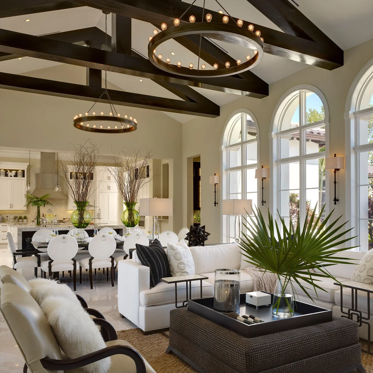Dark long-stem wall sconces with pale shades repeat on piers between arched windows in a large white living room.