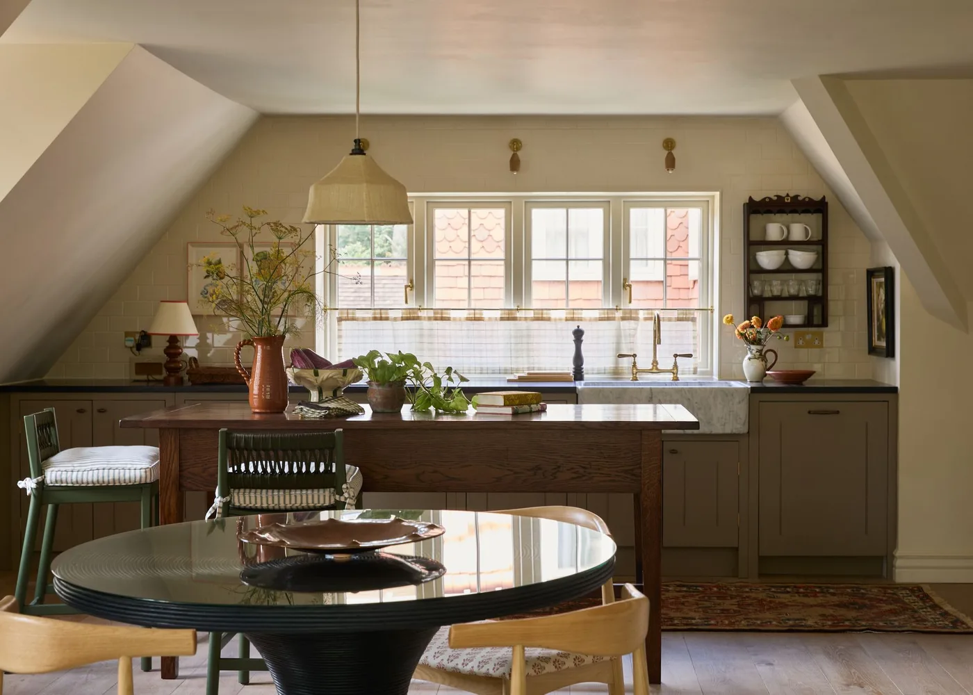 Attic kitchen with muted brown lower cabinets, a wood island, pale sloping walls and a round dining table.