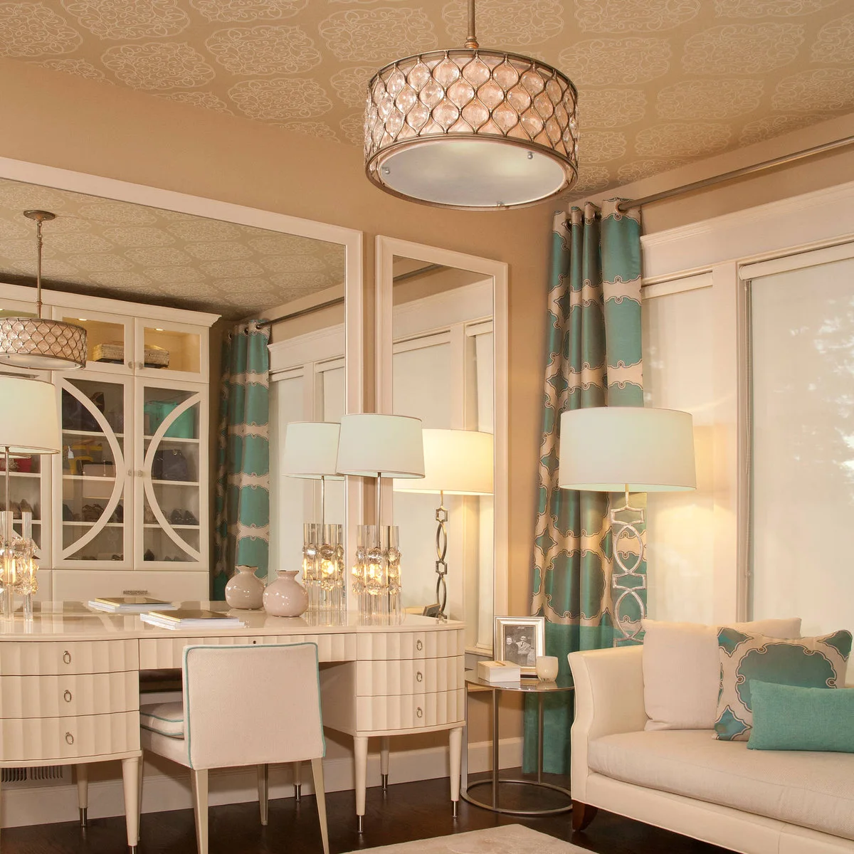 A long pale vanity with side drawers and a chair sits below a broad mirror beside turquoise curtains