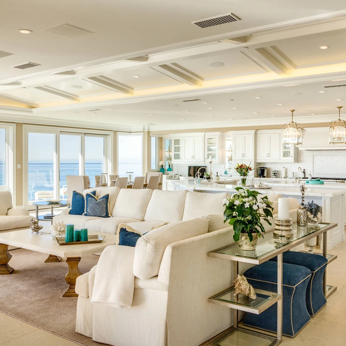 A pale sofa has a slim glass-topped console behind it, with two blue upholstered stools tucked underneath.