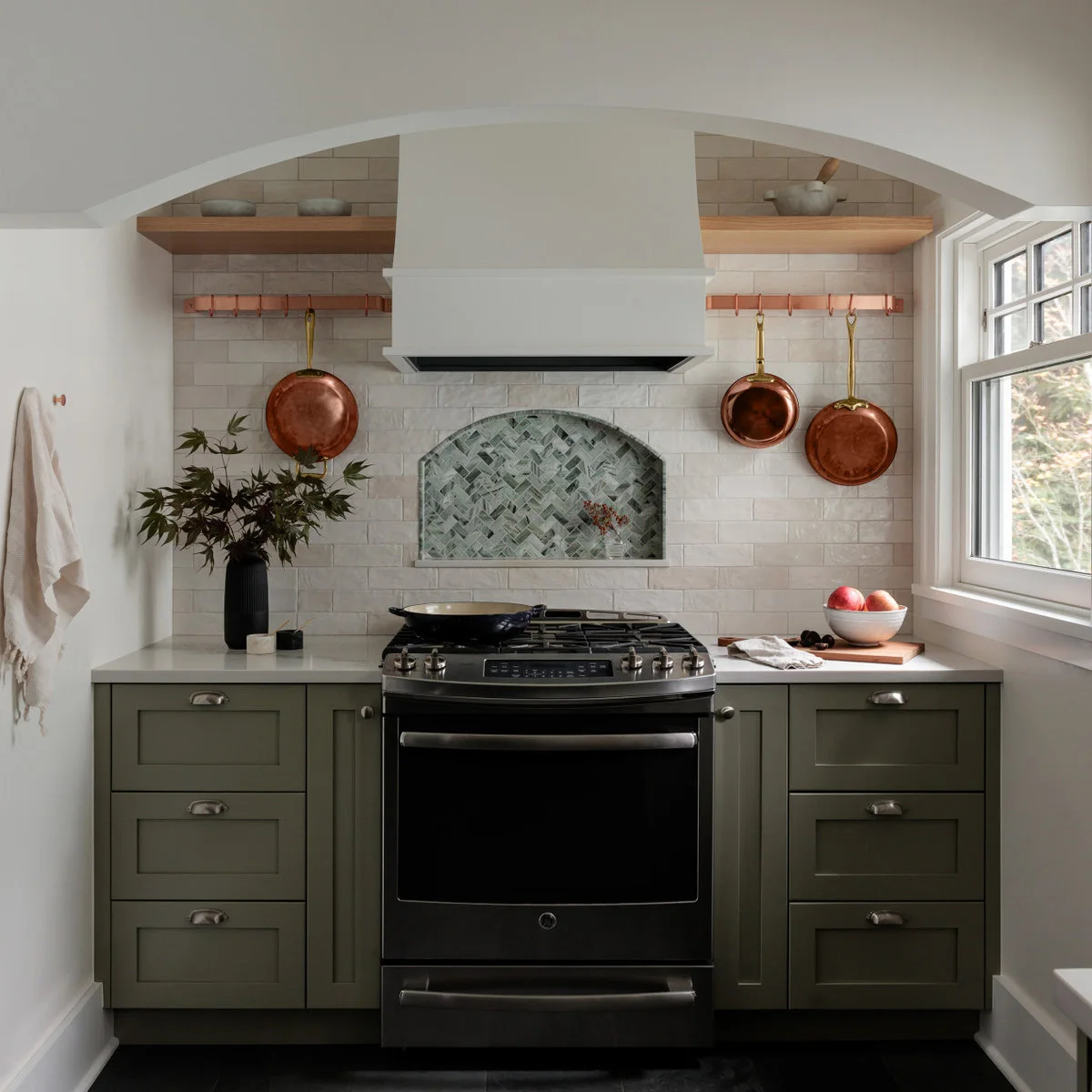 Compact green kitchen range wall with a tiled niche and copper-colored hanging pans