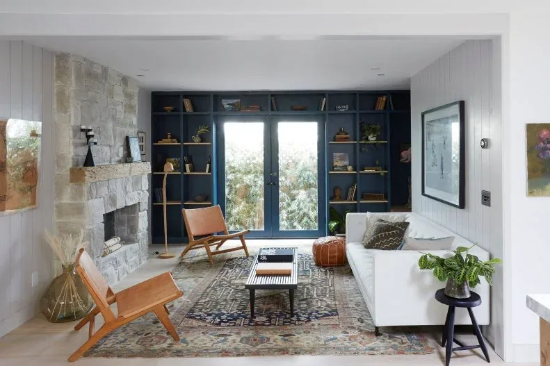 Narrow country living room with deep blue shelving around glazed doors, white sofa, wood-framed chairs and layered patterned rugs