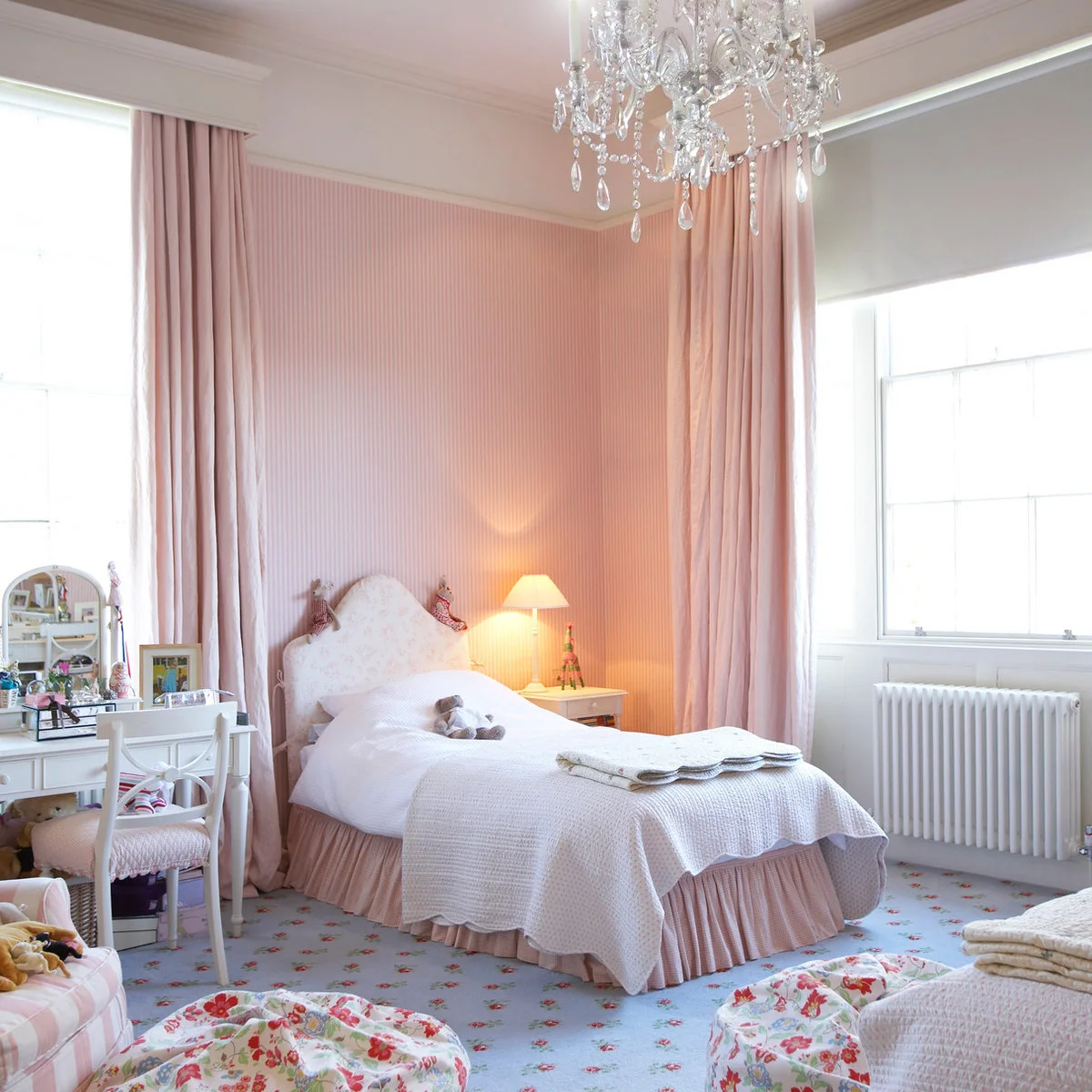 Single bed framed by long pink curtains, striped wall covering and white bedding