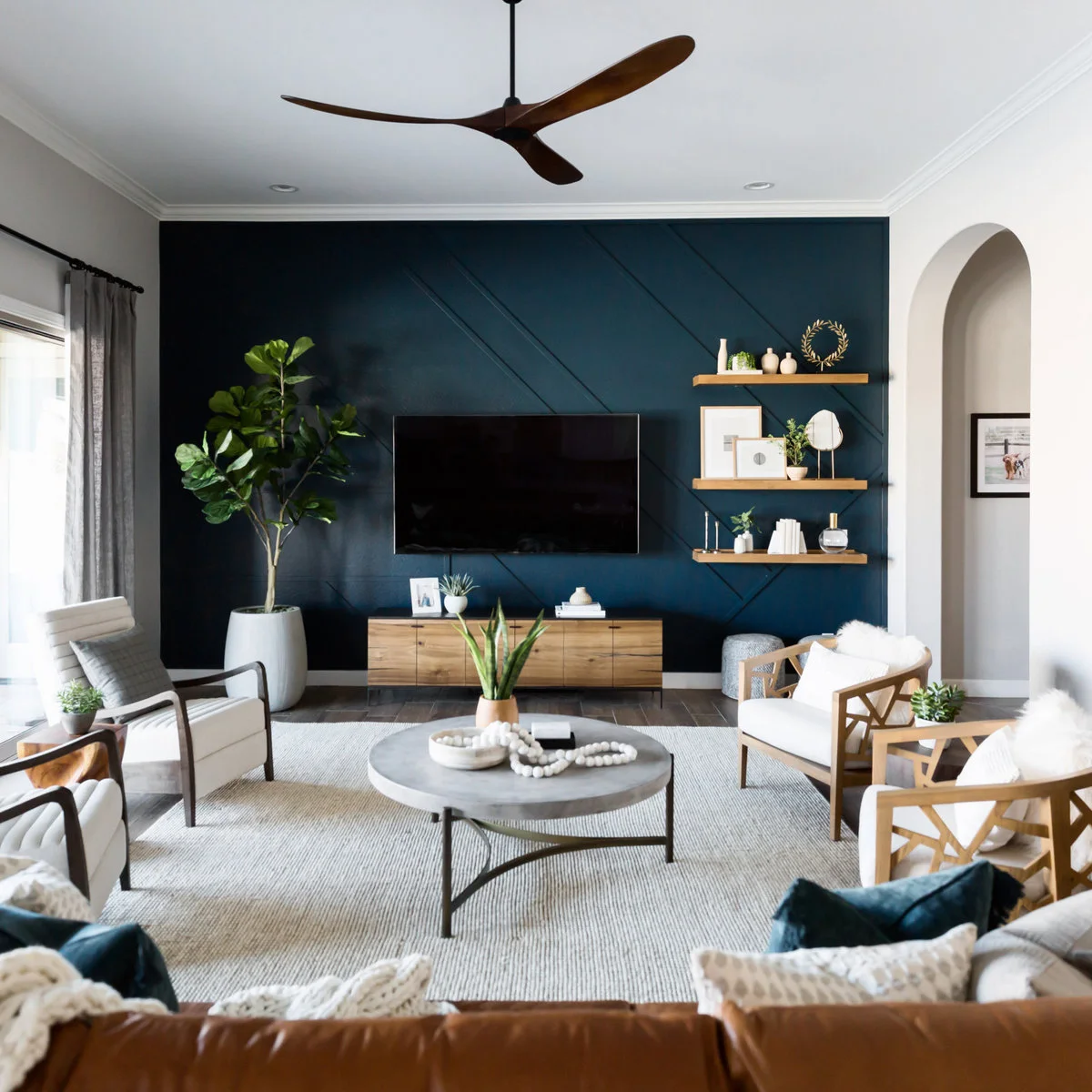 TV on a dark blue wall with diagonal trim, wooden console and shelves to one side