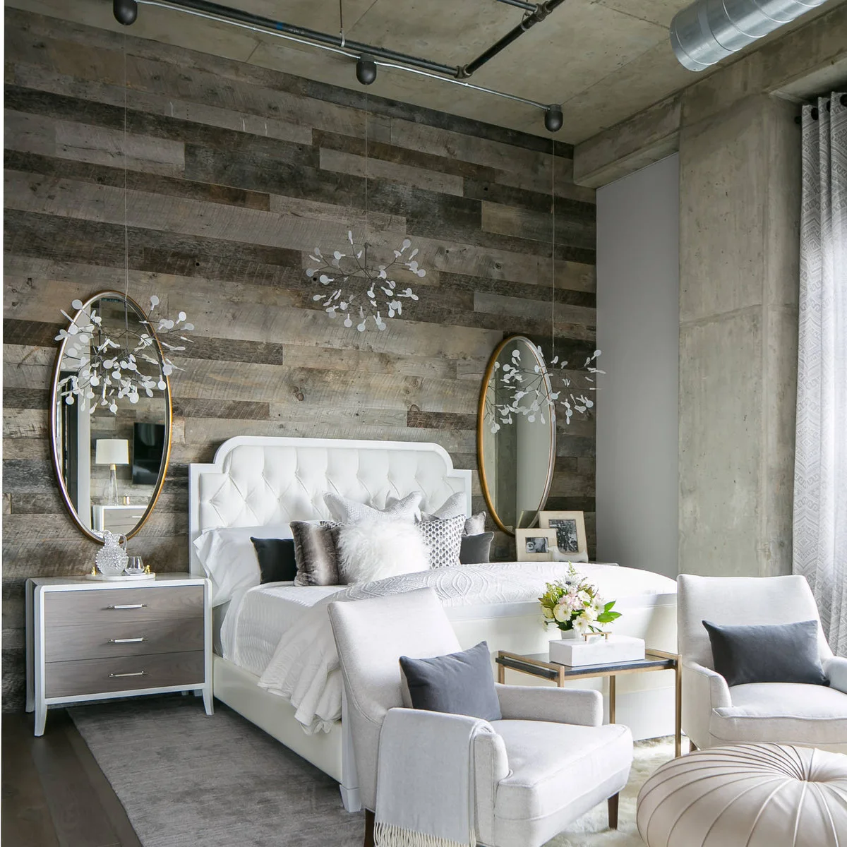Two decorative pendants hang beside a white bed against a wood-clad wall, with matching drawer chests and oval mirrors.
