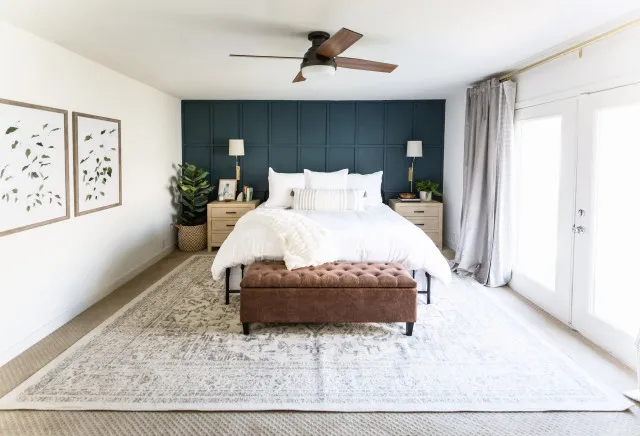 A brown upholstered bench sits at the foot of a white bed against dark blue paneling.