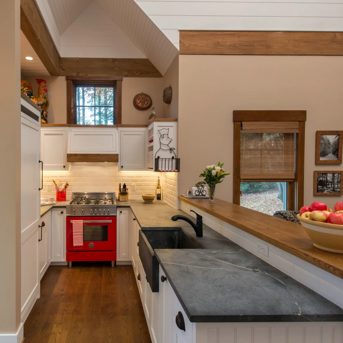 A wood-topped half wall runs behind a dark sink counter in a small white kitchen with a red range.