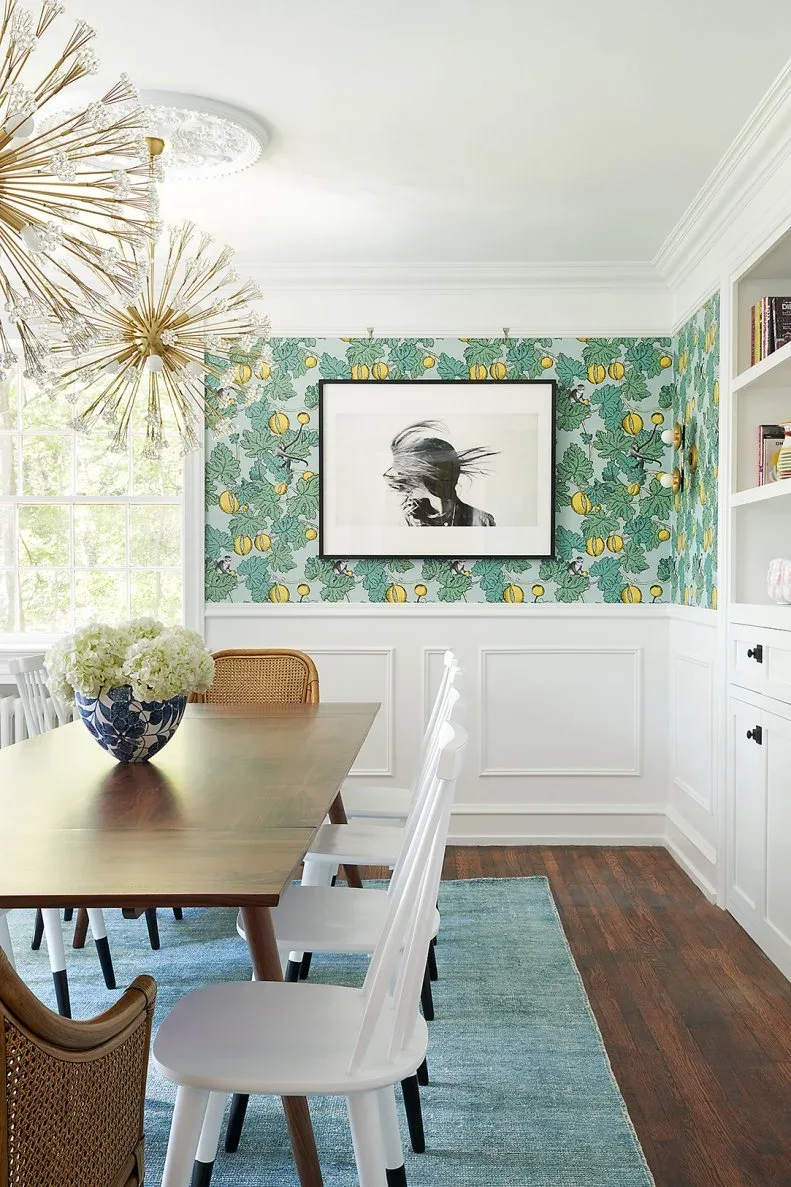 White rectangular wall panels beneath green and yellow patterned wallpaper beside a wood dining table