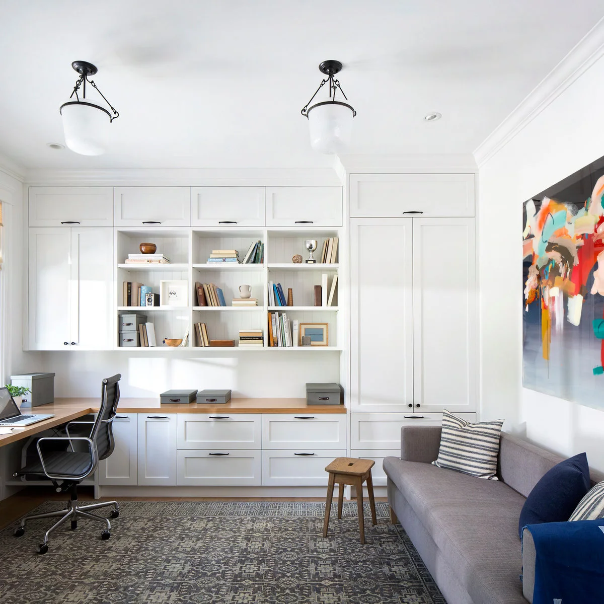 White fitted cabinets and a corner desk beside a gray sofa, with open shelves and a few storage boxes.