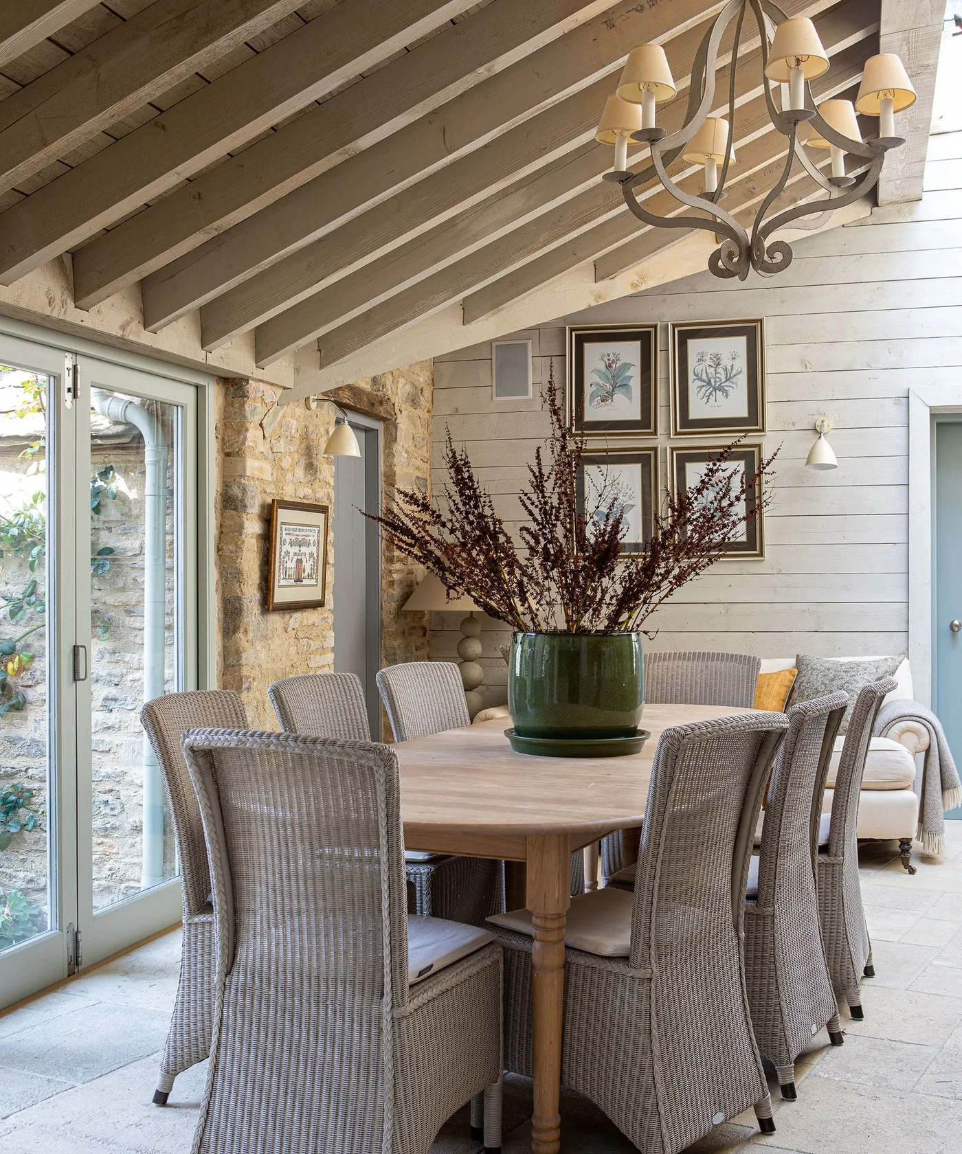 Dining room with horizontal pale wall boards, a boarded sloped ceiling, wood table and woven chairs