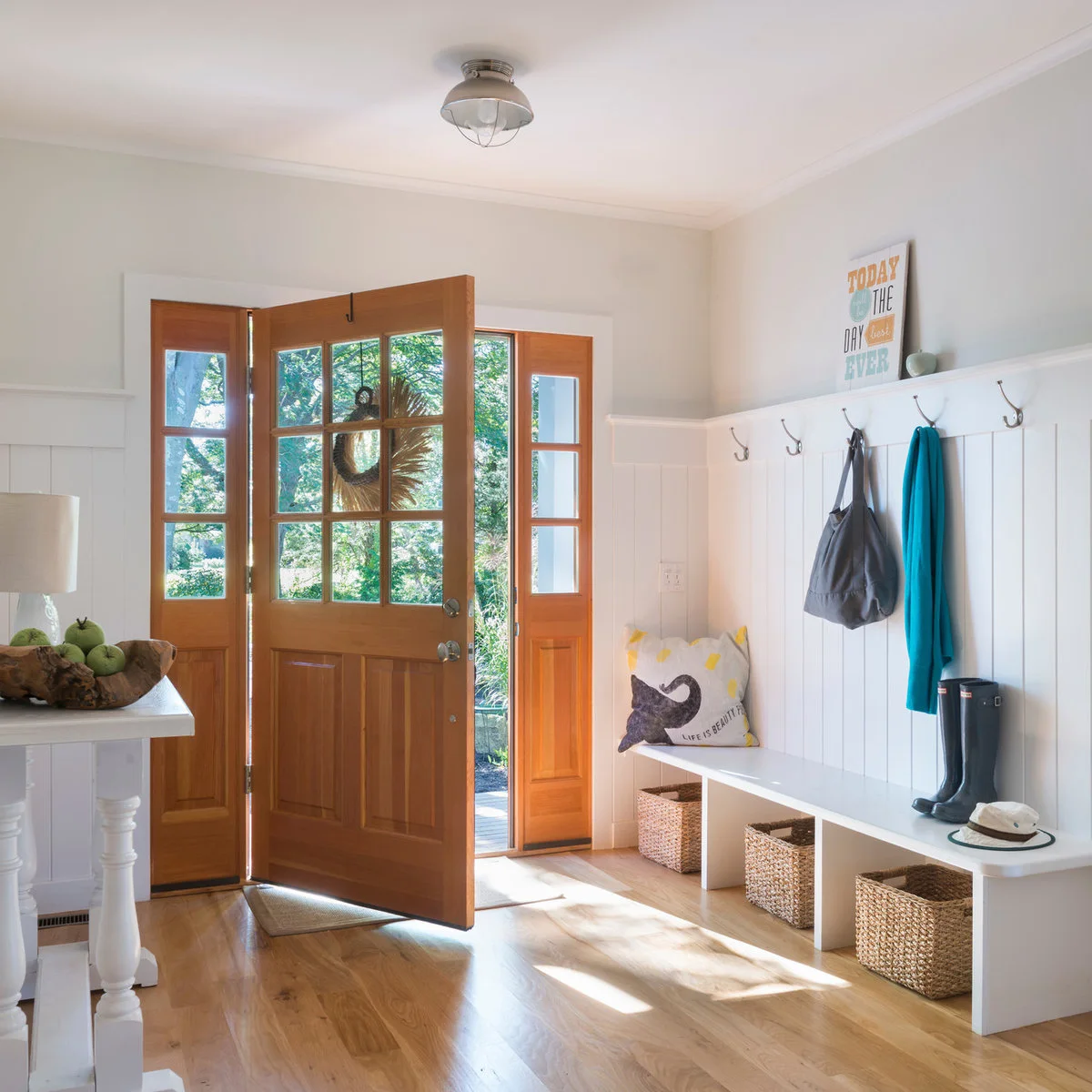 Compact white entry with a glazed wooden front door, wall hooks and a bench with three baskets underneath.