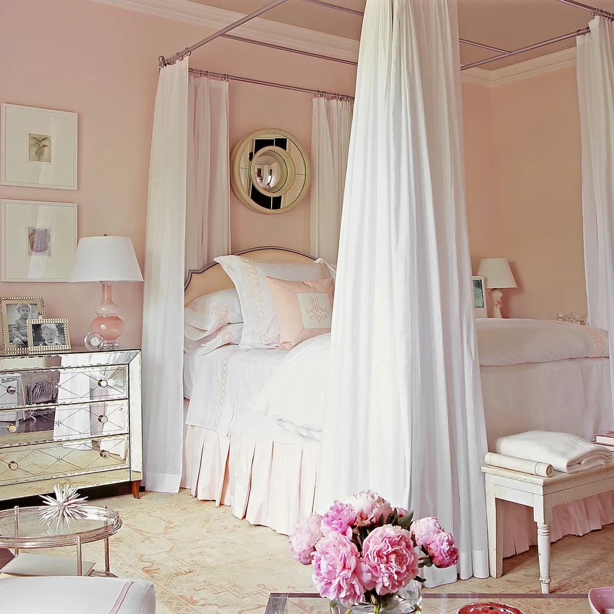 Pale pink bedroom with a canopy bed, white curtains, mirrored bedside chest and round gold-framed mirror