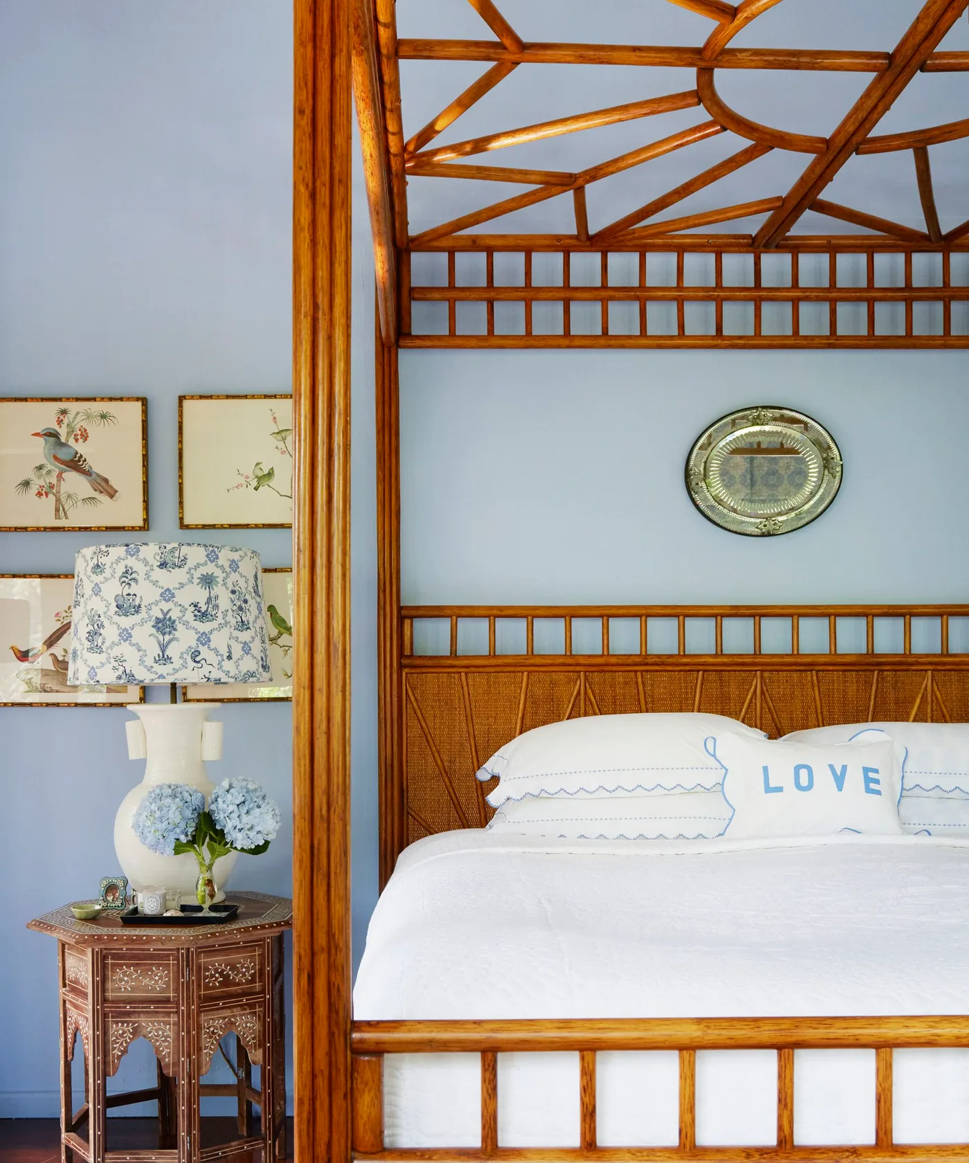 Pale blue walls around a wooden four-poster bed with white bedding and blue-edged pillows.