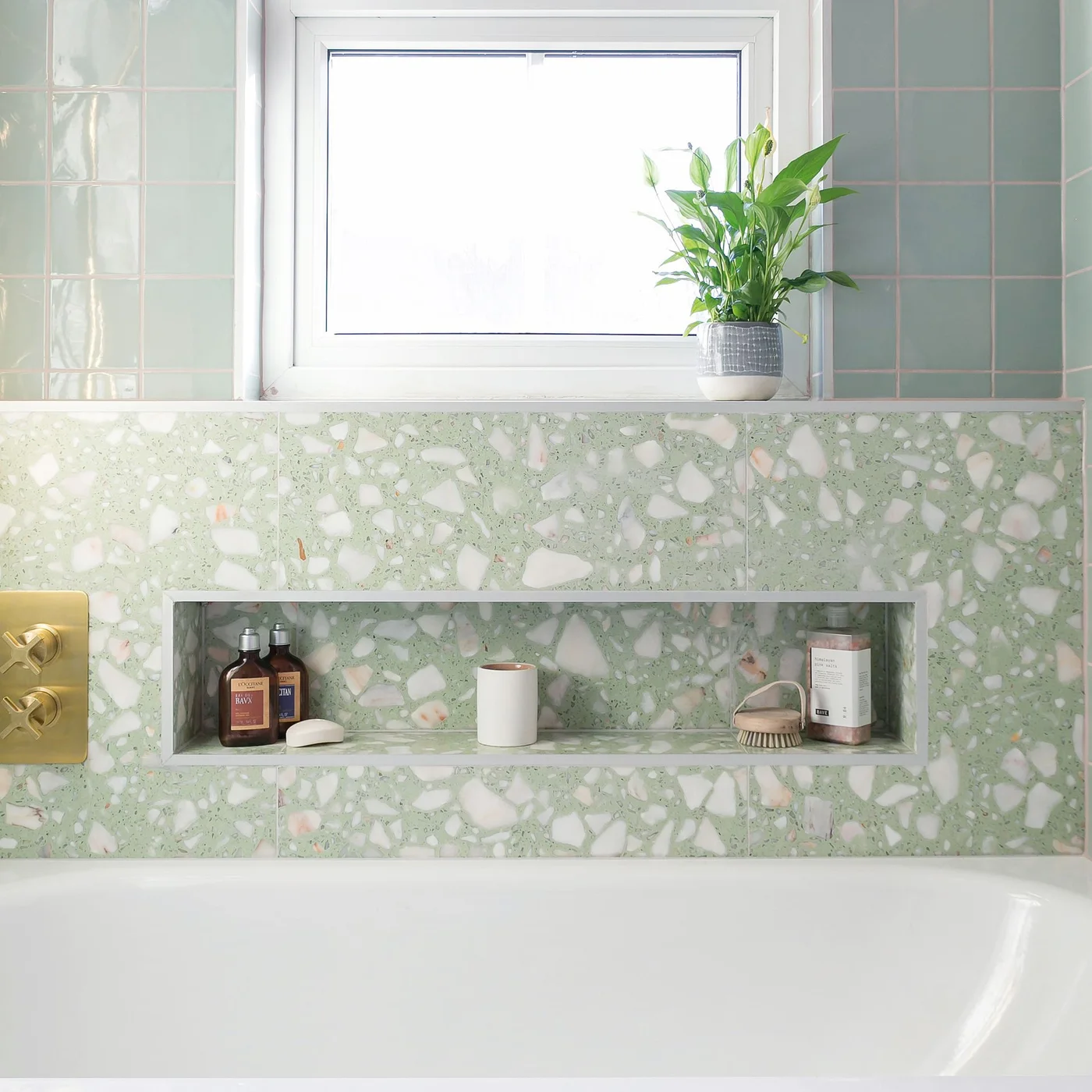 A green terrazzo wall contains a long bath niche below a window and green rectangular tiles.