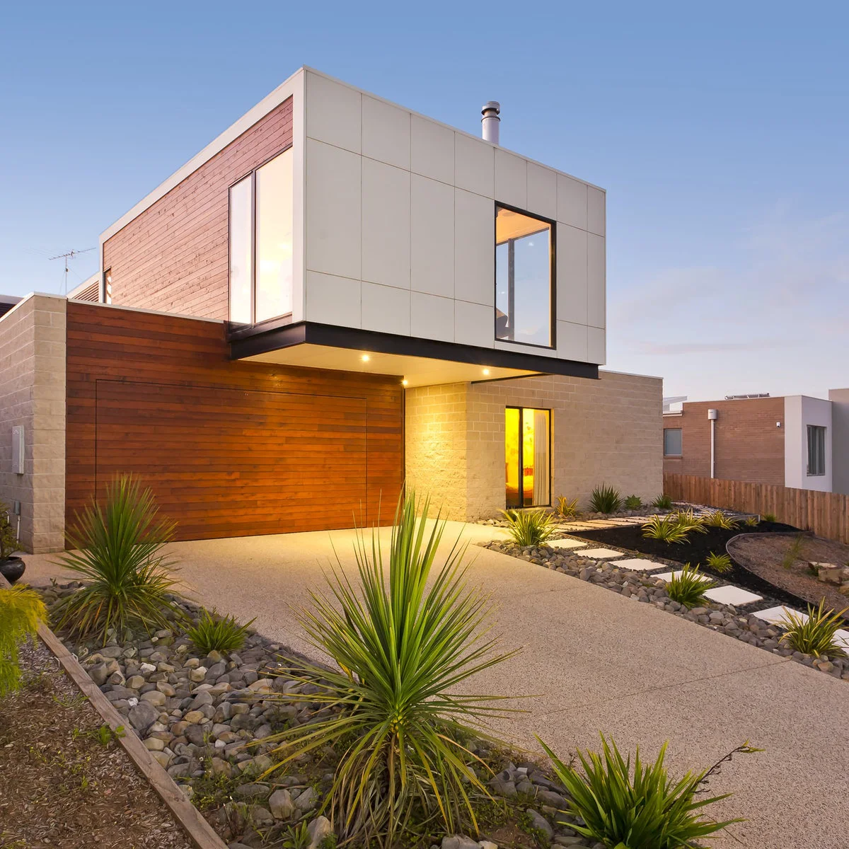 Concrete driveway toward a timber garage door with a separate stepping-slab path, stones and spiky planting beside it.