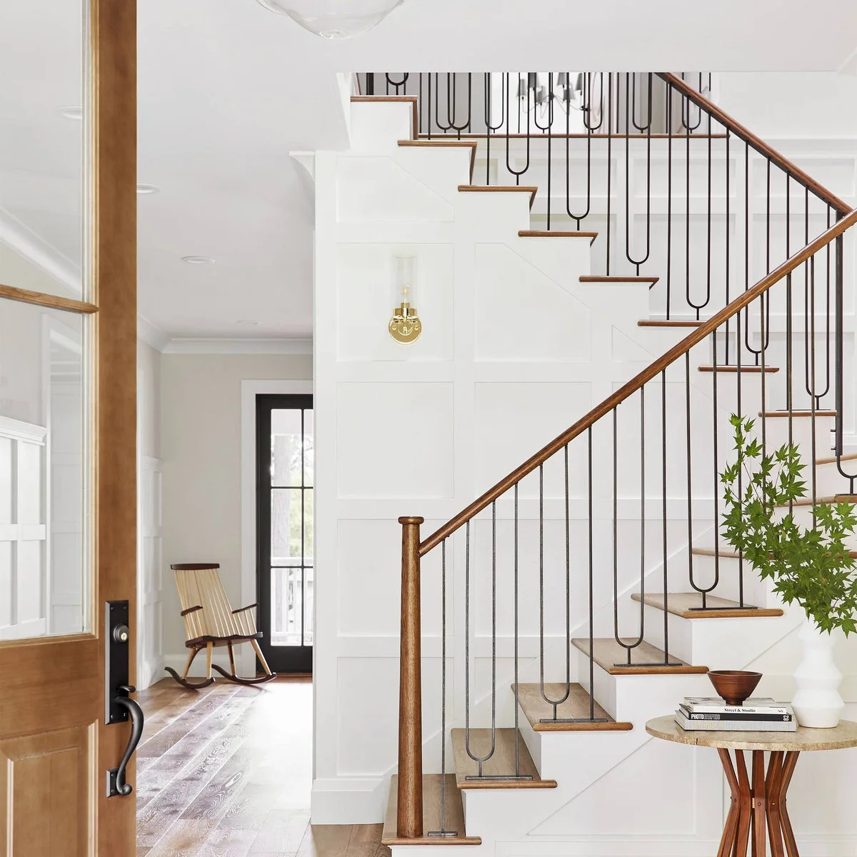 White staircase with wood treads and handrail, slim dark looped balusters and paneled walls