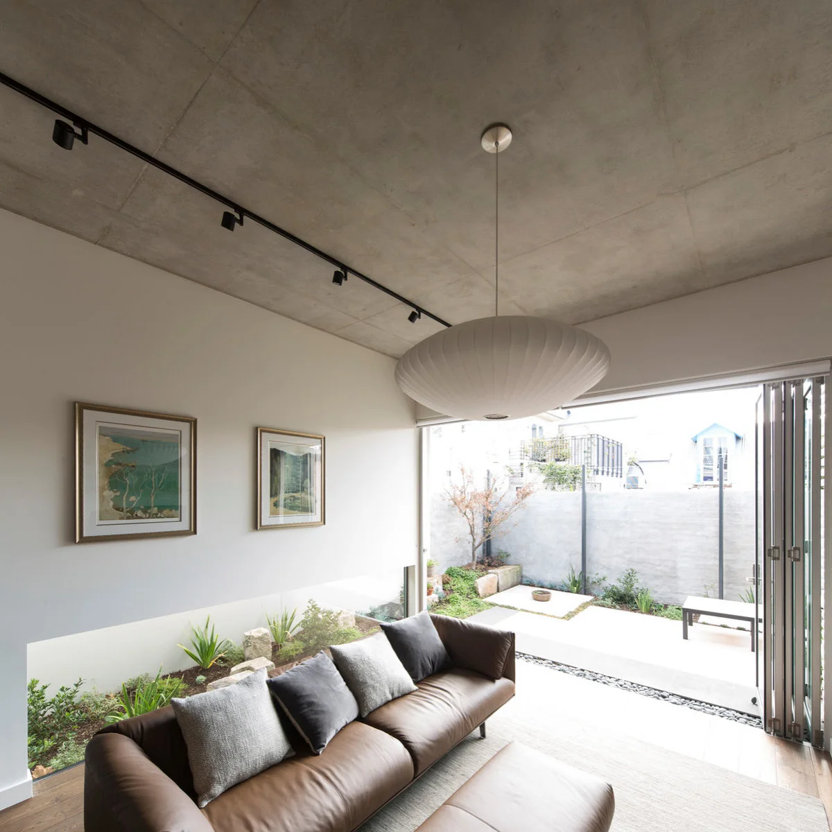 Terrace living area with a long brown sofa, pale oval pendant and folding doors to a small garden