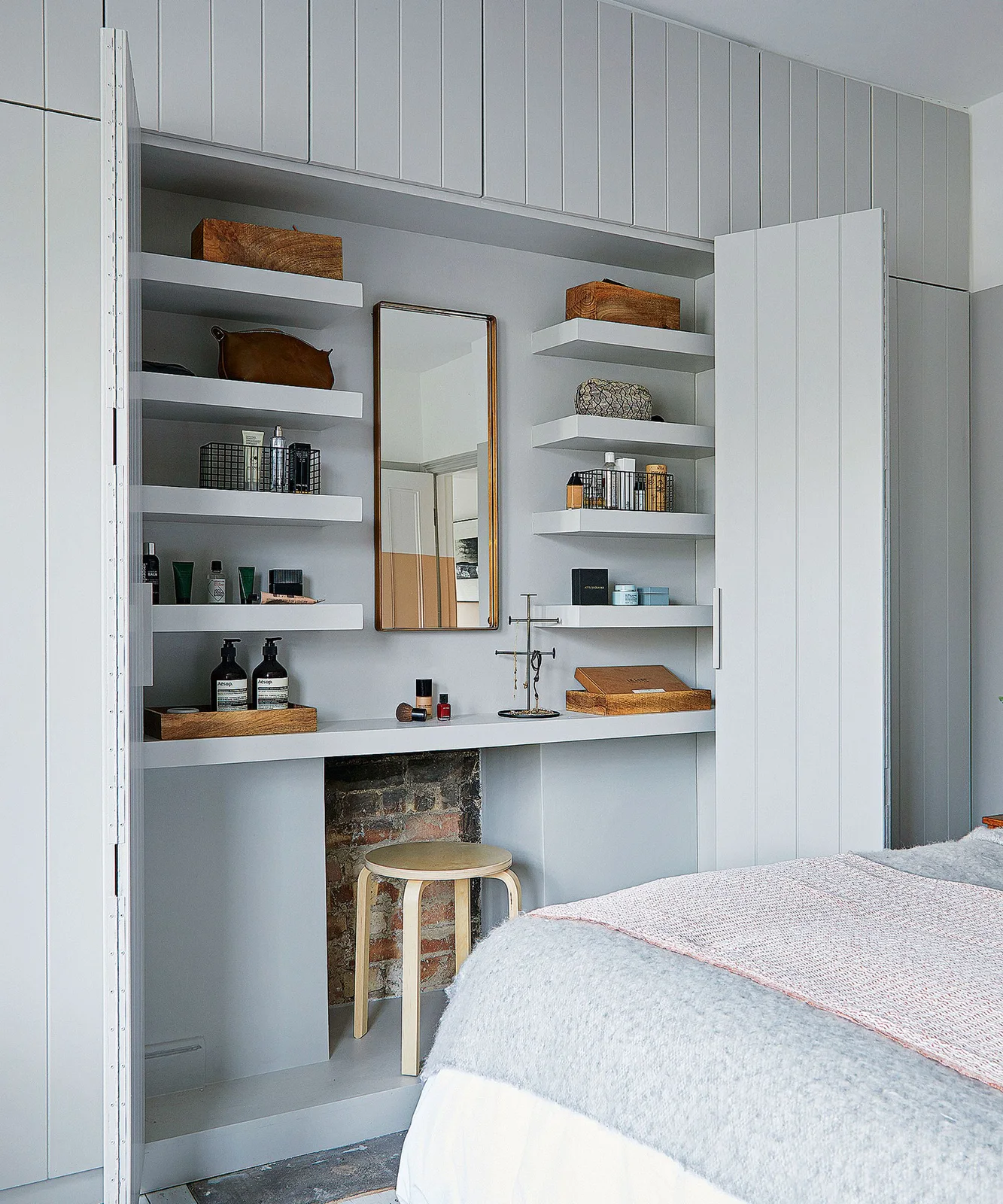 Gray paneled doors open onto a dressing counter with a tall mirror, shallow side shelves, small trays and a stool that fits beneath.
