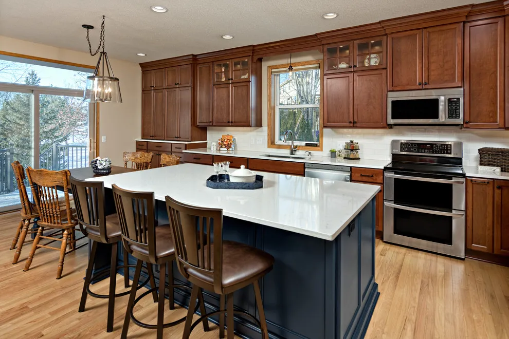 Warm wood perimeter cabinets surround a deep blue island with a pale worktop