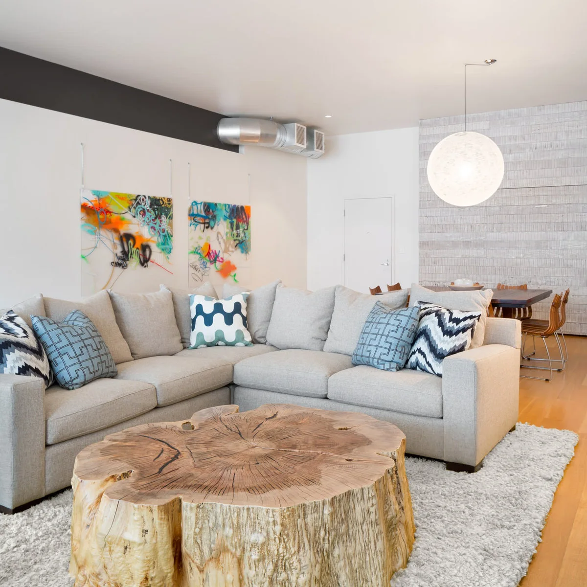 Large wood-slice coffee table left bare beside a pale sectional and colorful wall art