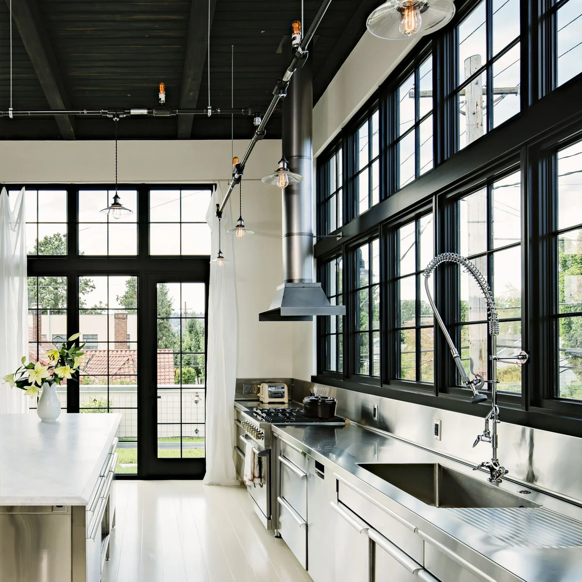 White curtains at black-framed kitchen doors beside stainless-colored counters