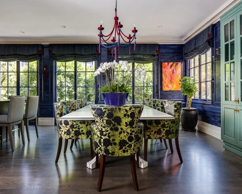 Dark gathered window shades above black-framed dining windows with patterned chairs and a pale table