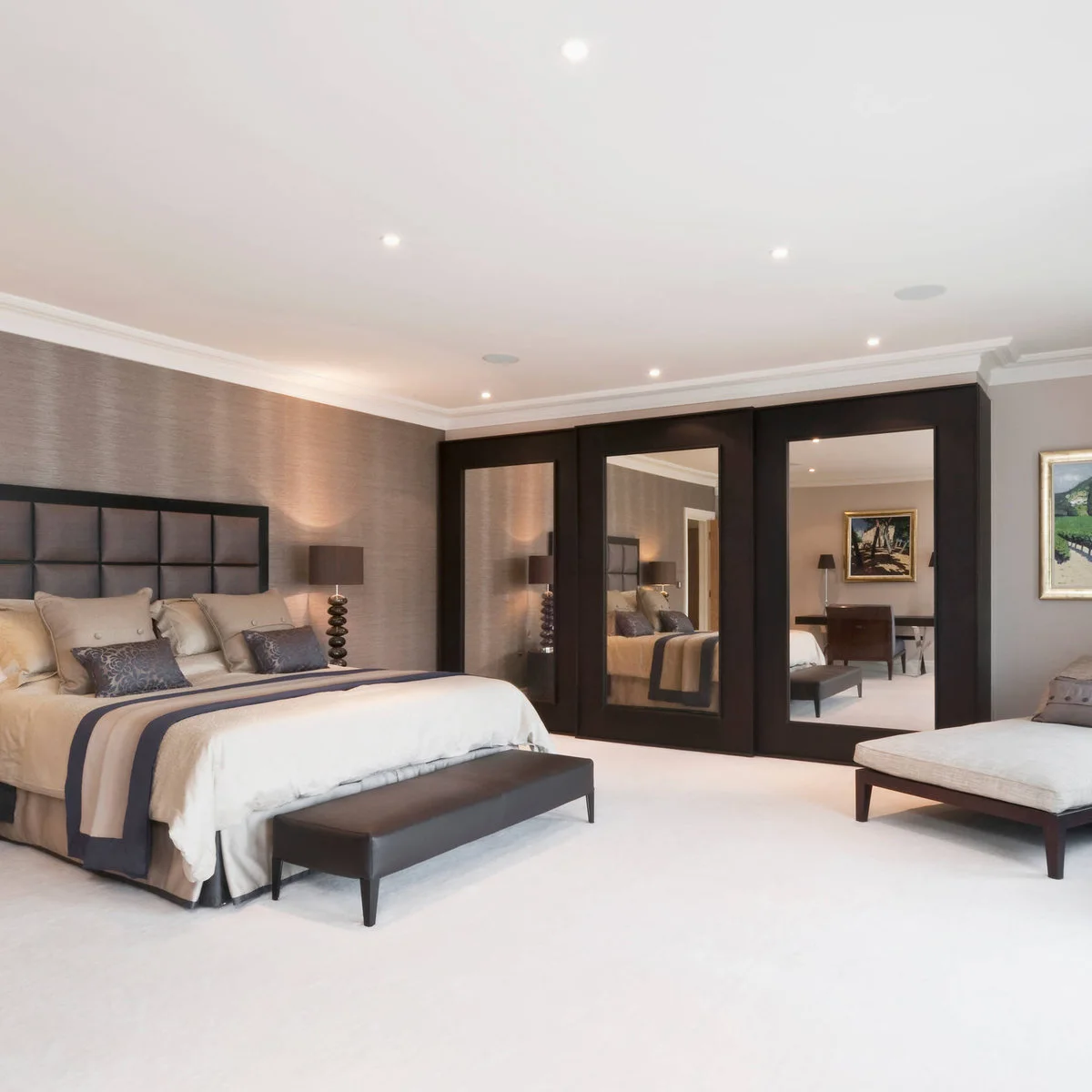 Dark brown mirrored wardrobes beside a bedroom with pale carpet, neutral bedding and a low brown bench.