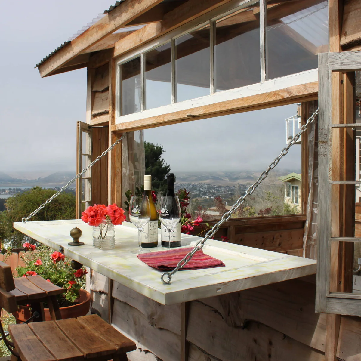 Fold-down pale counter supported by chains at a rustic shed window with two stools