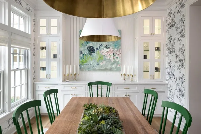 White vertical wall paneling between glazed dining cabinets behind green chairs and a wood table