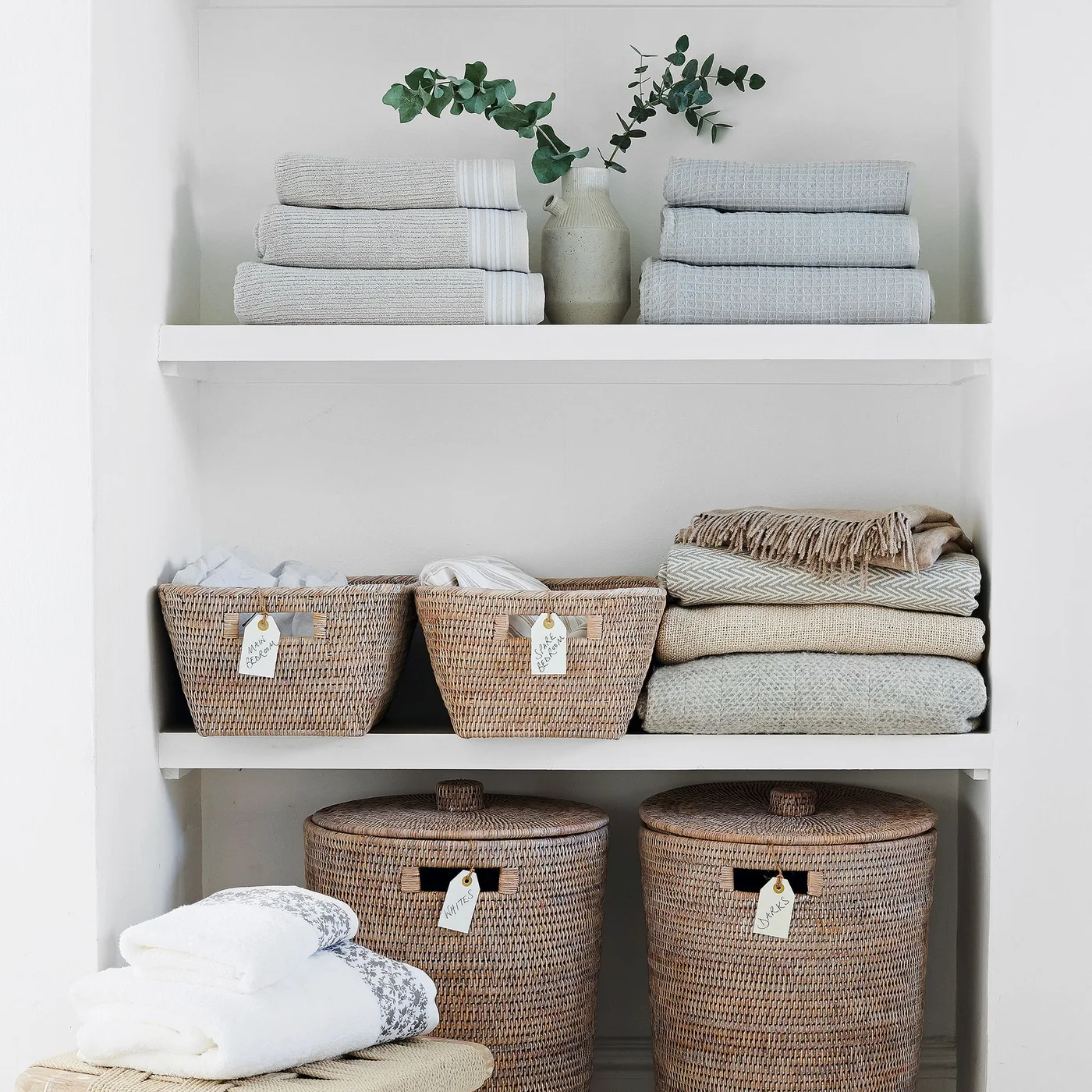 White linen shelves with labeled woven baskets, folded blankets, towels and two round laundry baskets