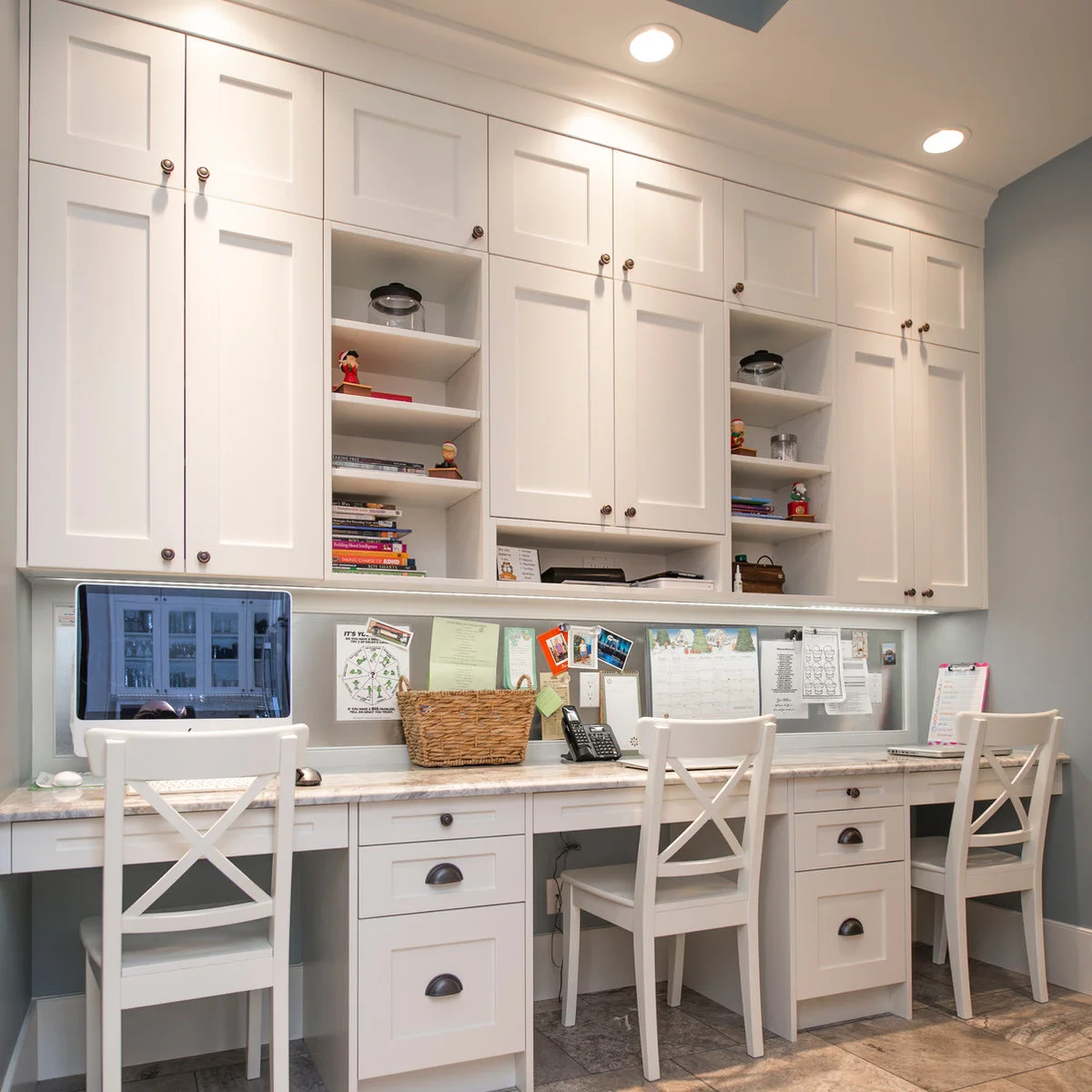 Long fitted white desk with three chairs, drawer pedestals, overhead cupboards and a continuous noticeboard