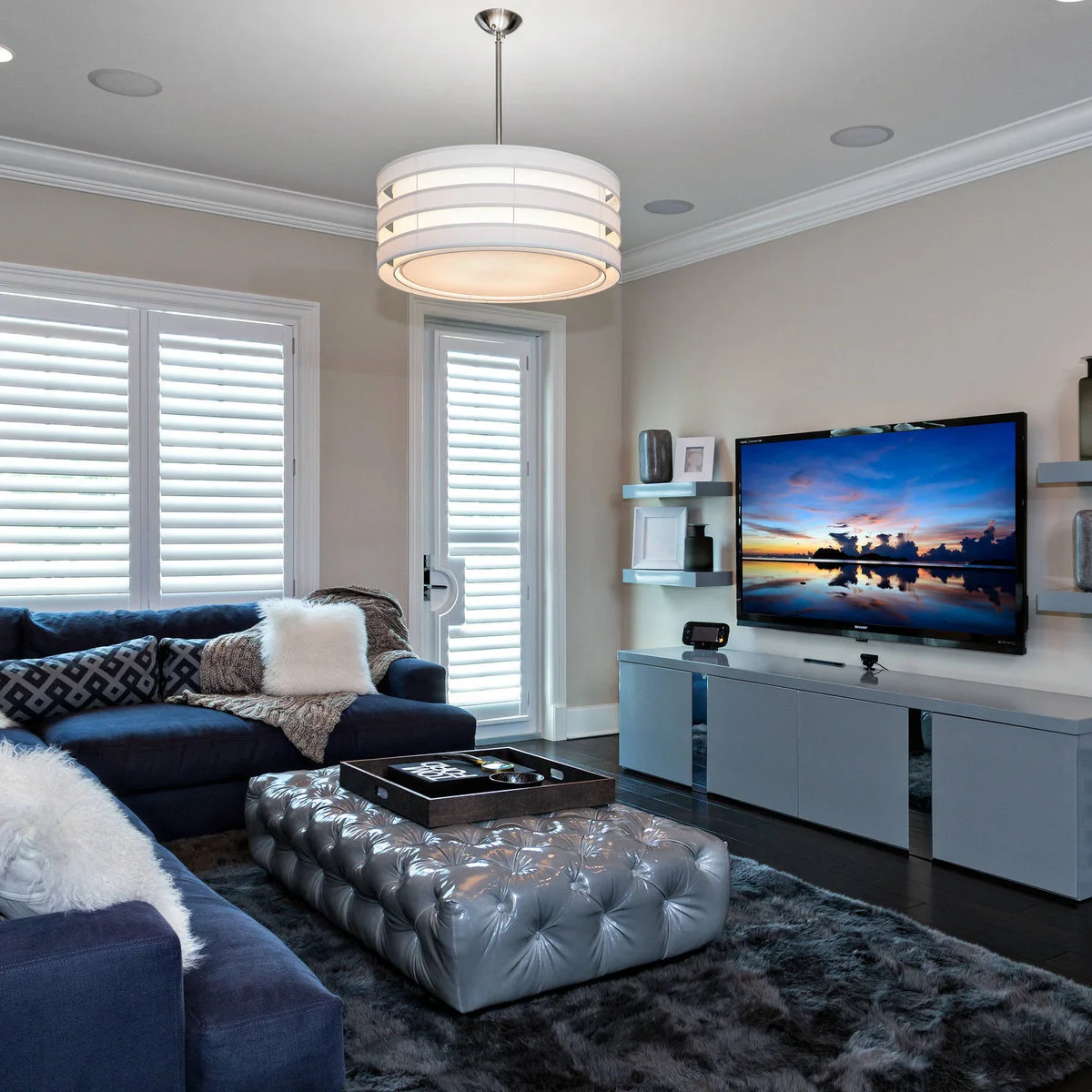 A gray media cabinet stays largely clear beneath a television while small vessels and frames occupy wall shelves at the sides.