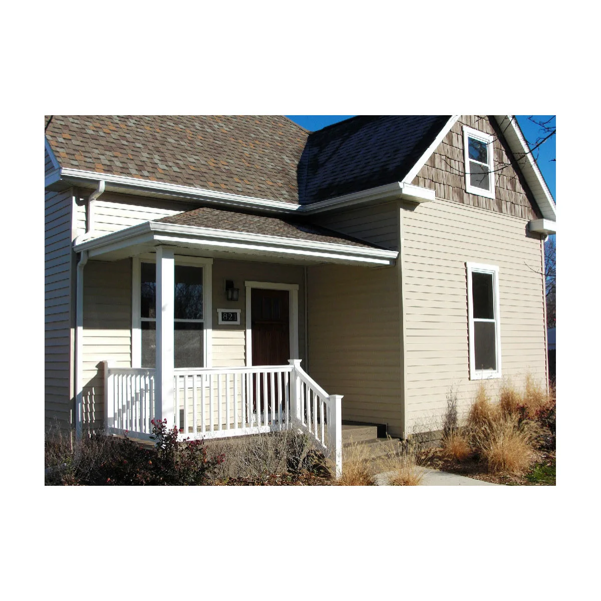 Small covered front porch with white railings, a dark door and a clearly visible house number