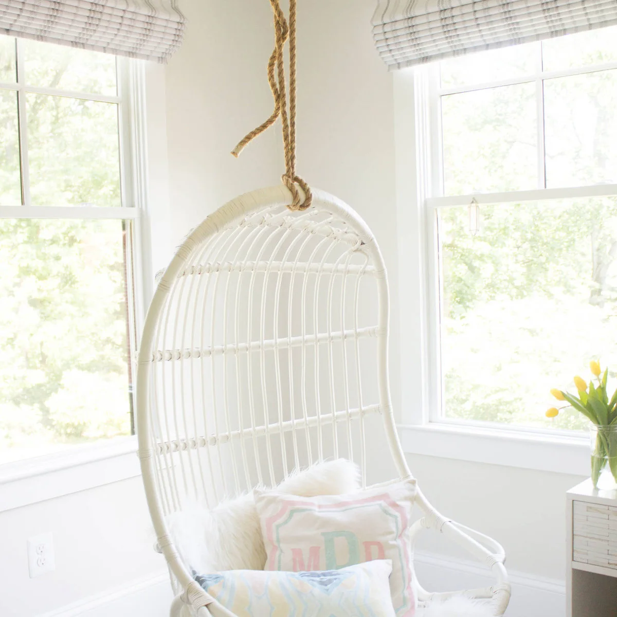 White hanging chair with pale cushions in a teen bedroom corner beside two windows
