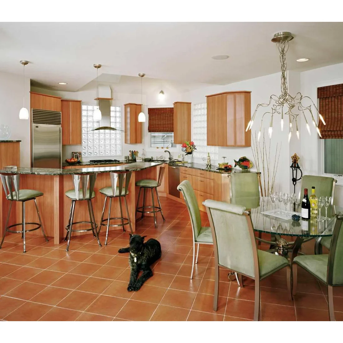 Terracotta squares spread between timber kitchen cabinets, bar stools and a glass dining table.