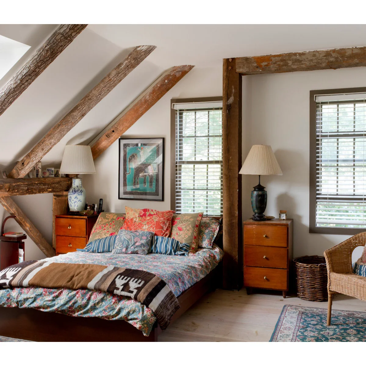 Bedroom beneath exposed timber beams with floral bedding, a brown geometric blanket and warm wood bedside chests
