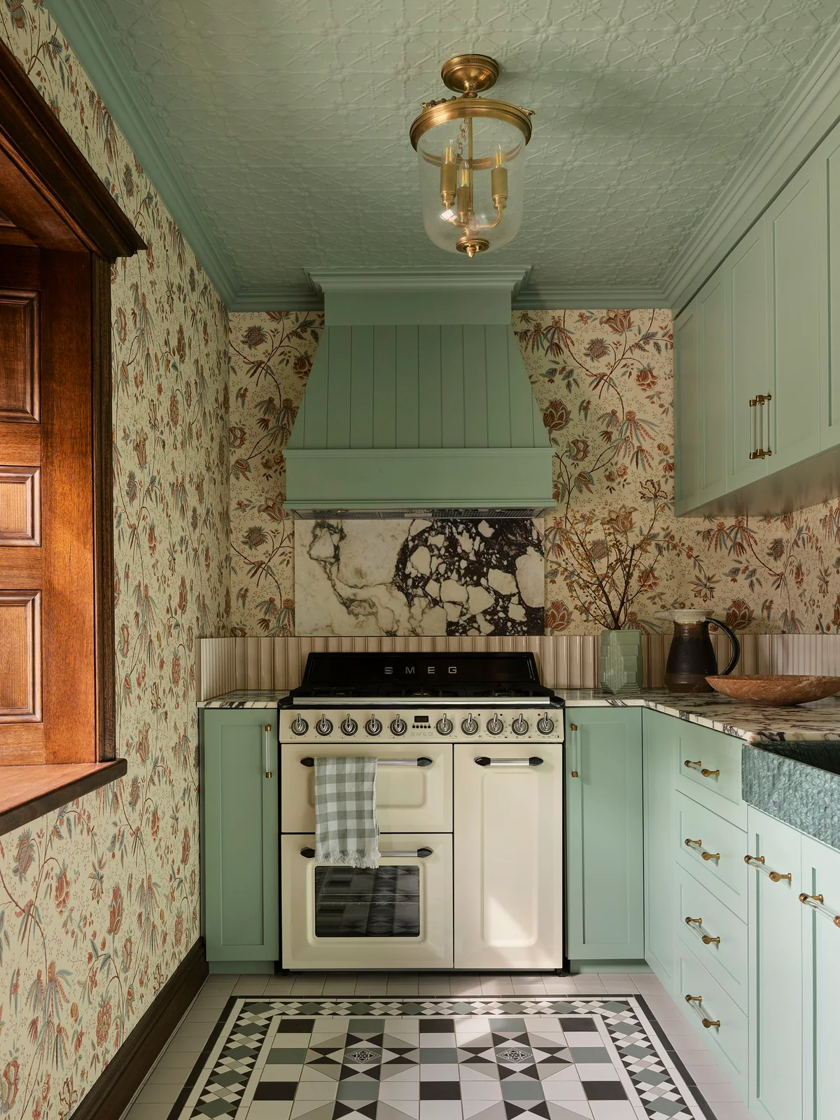 Floral kitchen walls surround pale green cabinets and a matching textured ceiling above a black-and-white patterned floor and strongly veined backsplash