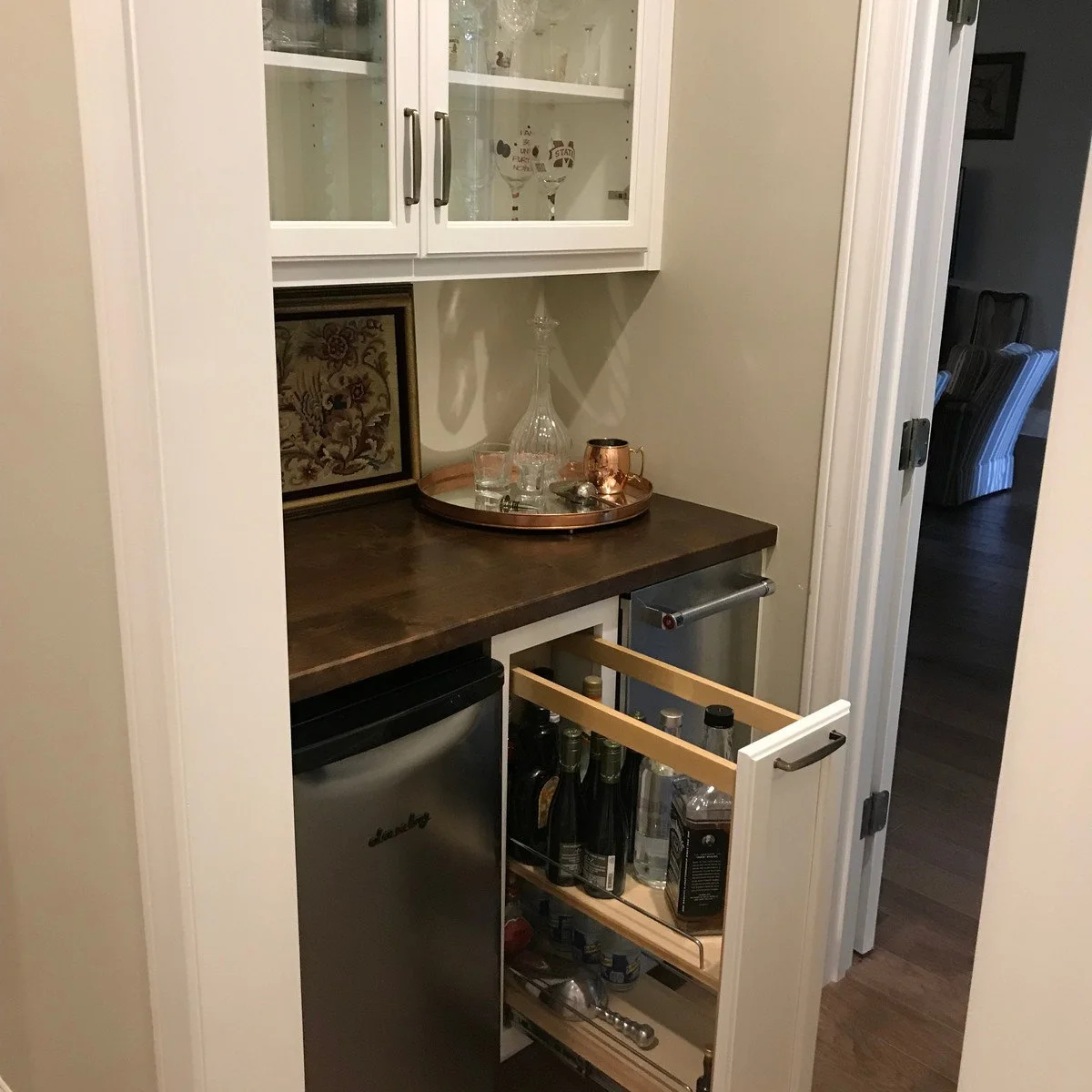 Compact bar with white upper cabinet, brown counter and narrow bottle pull-out between lower appliances