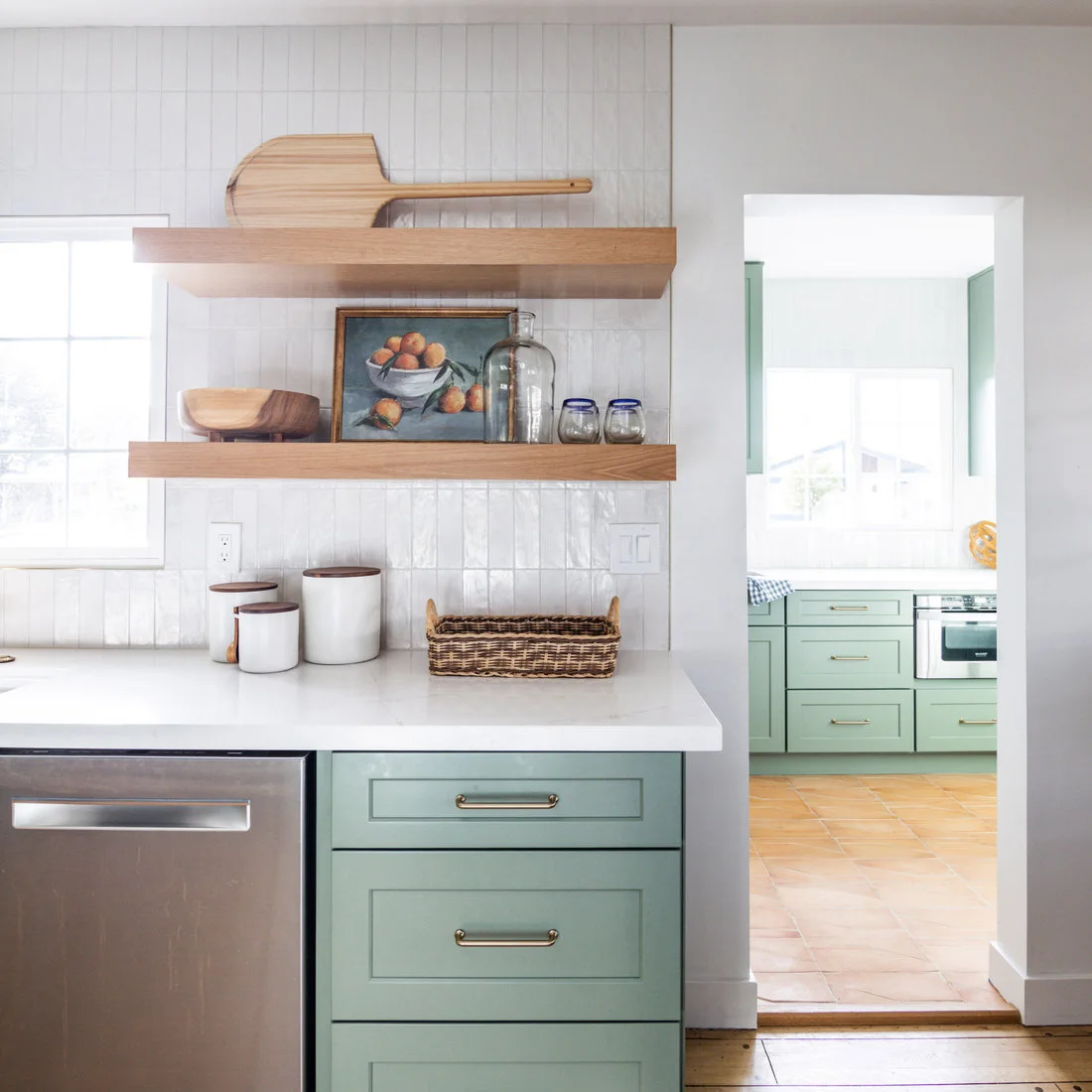 A timber threshold separates peach terracotta tiles from wooden boards in a pale green kitchen.