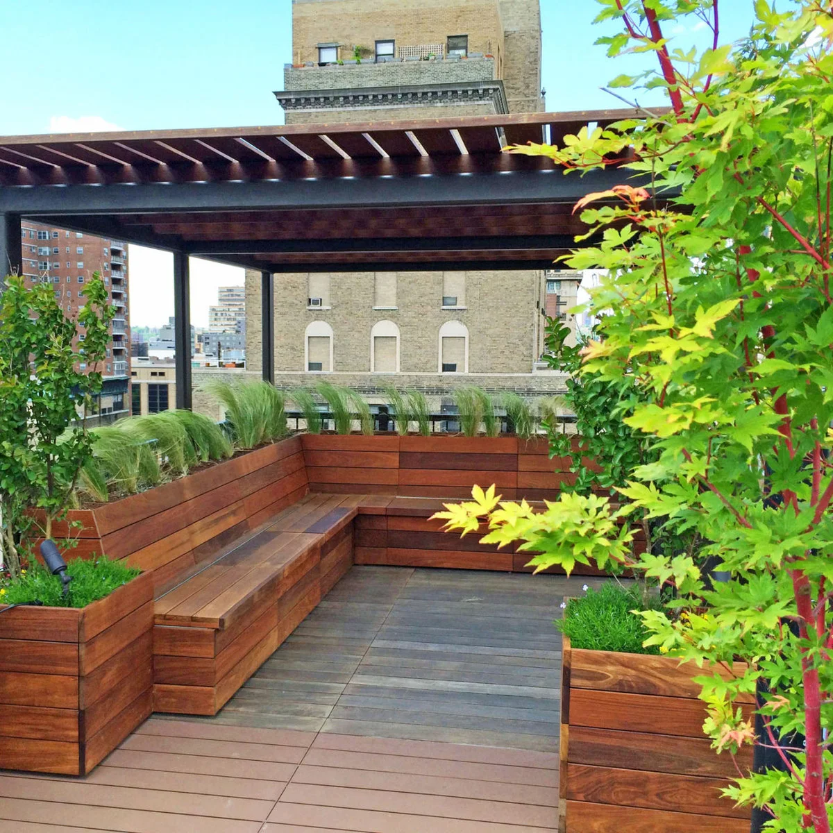 An L-shaped wood bench sits under a dark pergola between raised wood planters on a rooftop terrace.