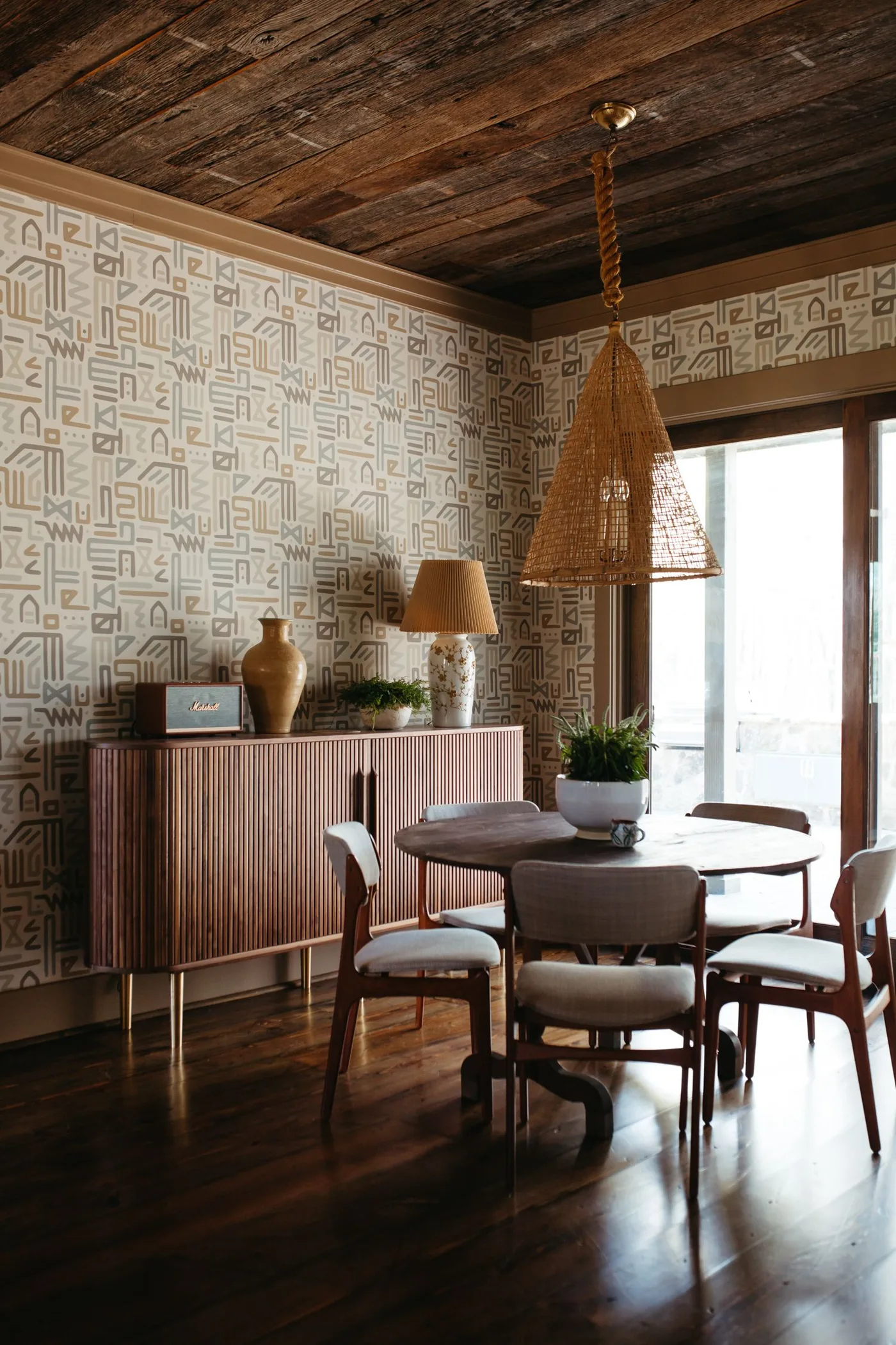 Wood ribbed sideboard on slender legs beside a dark round table under a woven pendant