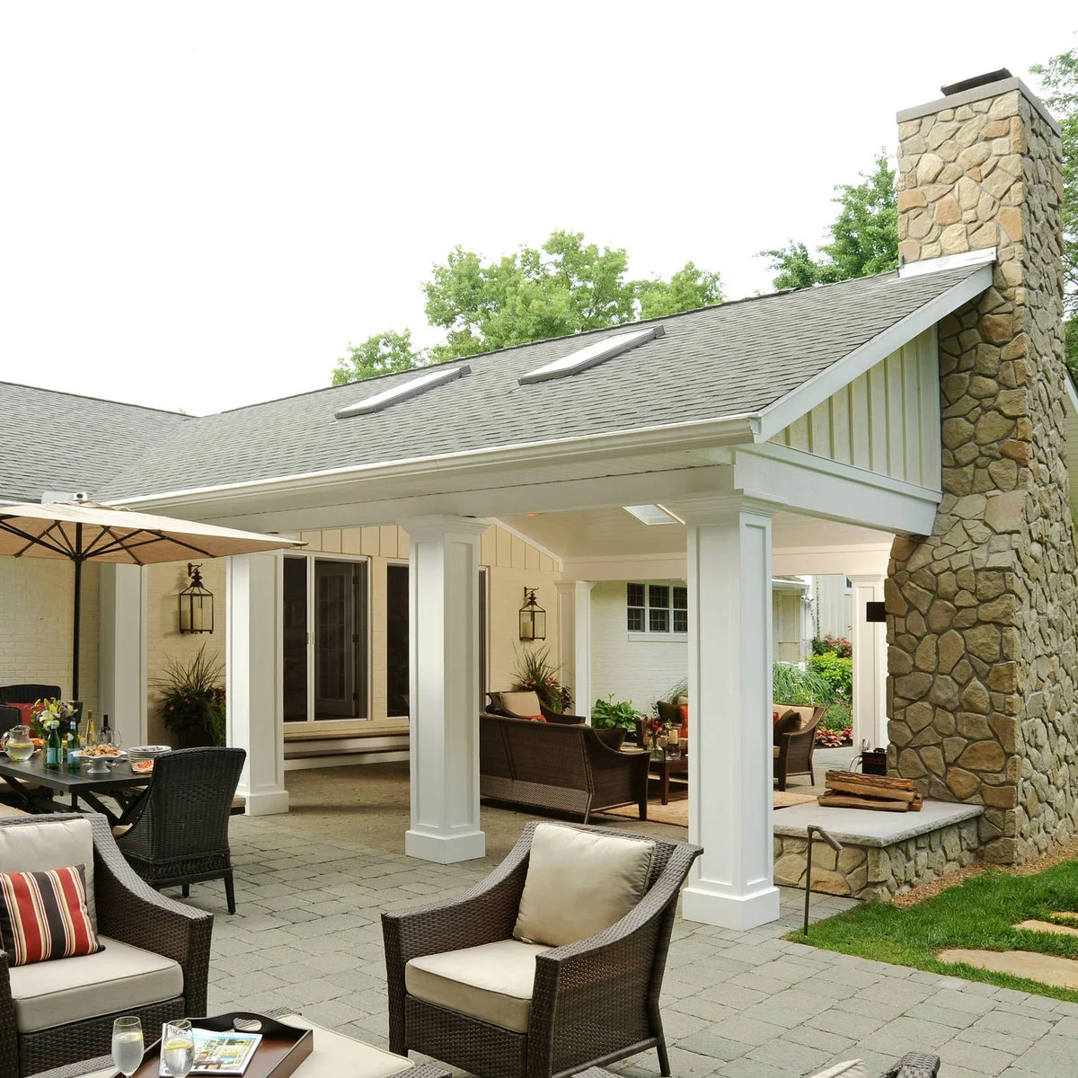 Two rooflights interrupt a pale pitched patio roof above lounge seating, with dining under an umbrella on the open terrace.