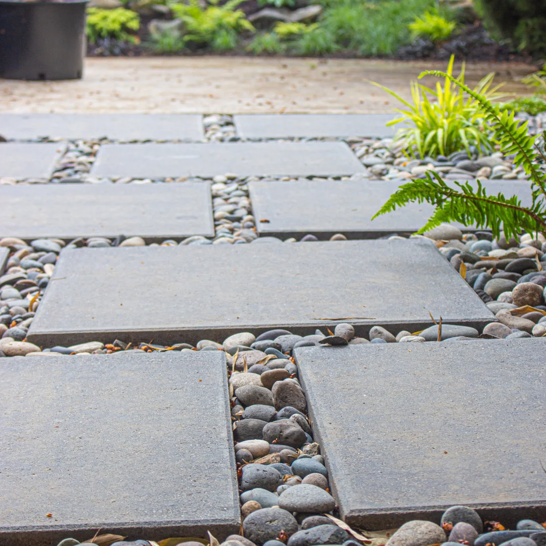 Gray rectangular paving slabs separated by smooth mixed-color stones beside green foliage