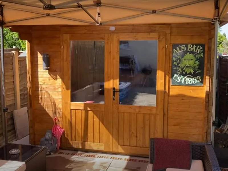 Wood garden pub entrance with glazed double doors, a hanging sign and seating under a canopy