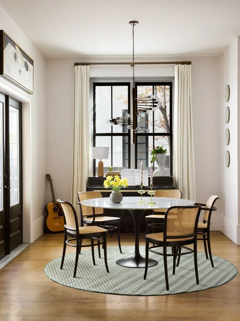 Round green patterned rug beneath a pale round dining table and black chairs with woven backs