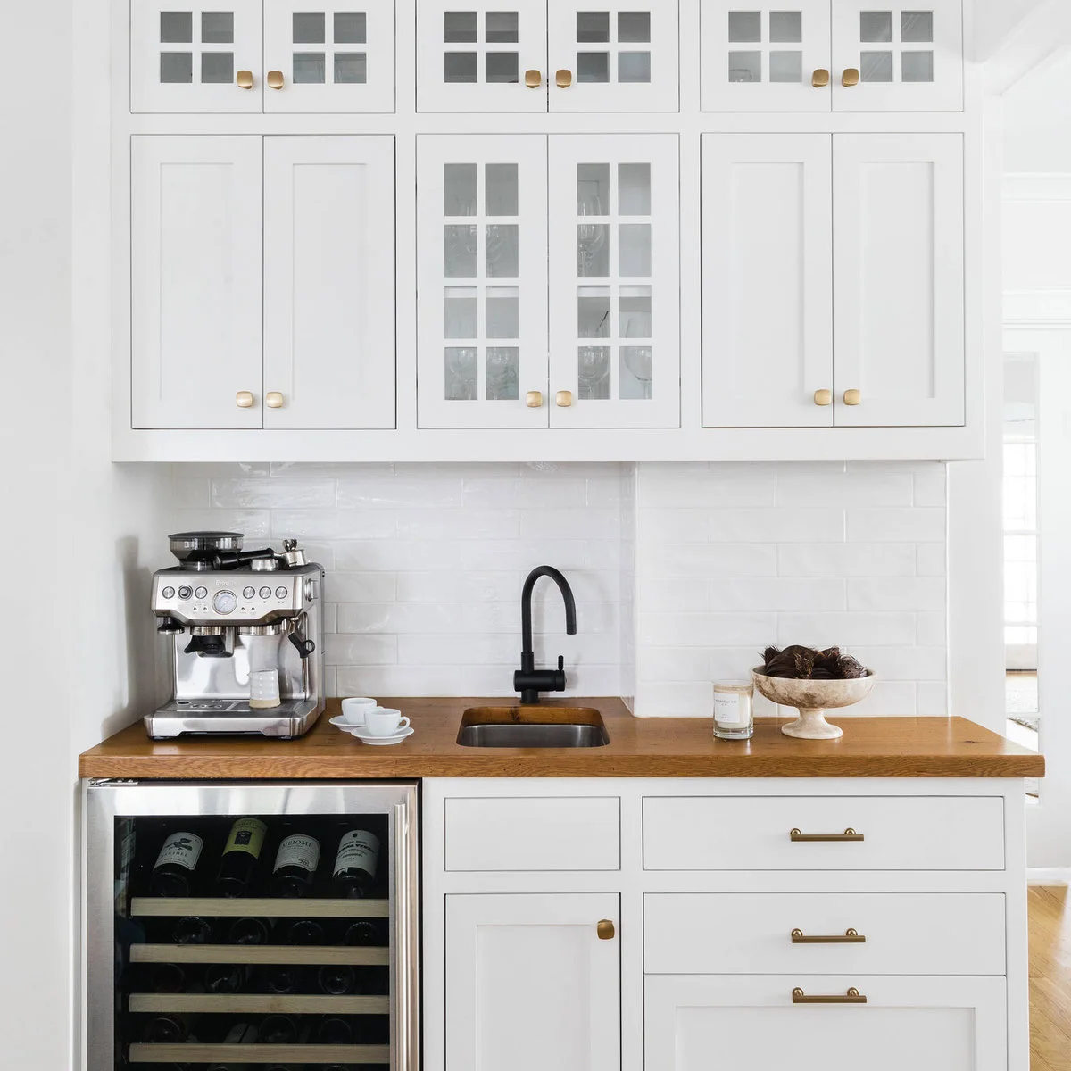 White beverage counter with espresso machine at one end, black faucet and wood-toned worktop