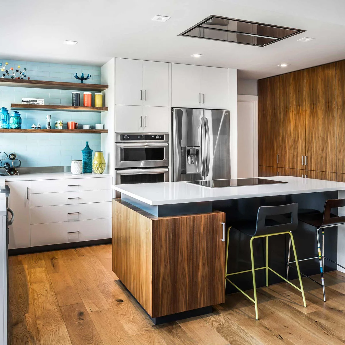 White and wood cabinetry with pale blue tile, open wood shelves and a few colorful containers beside an island.