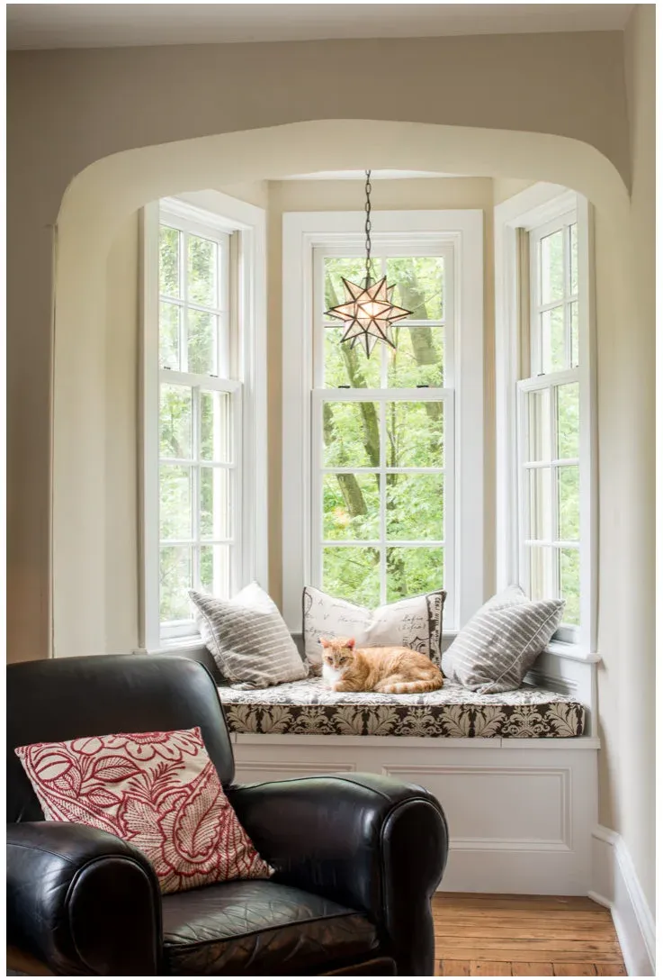 A cat rests on a patterned cushion in a narrow three-sided window recess beneath a star-shaped pendant.
