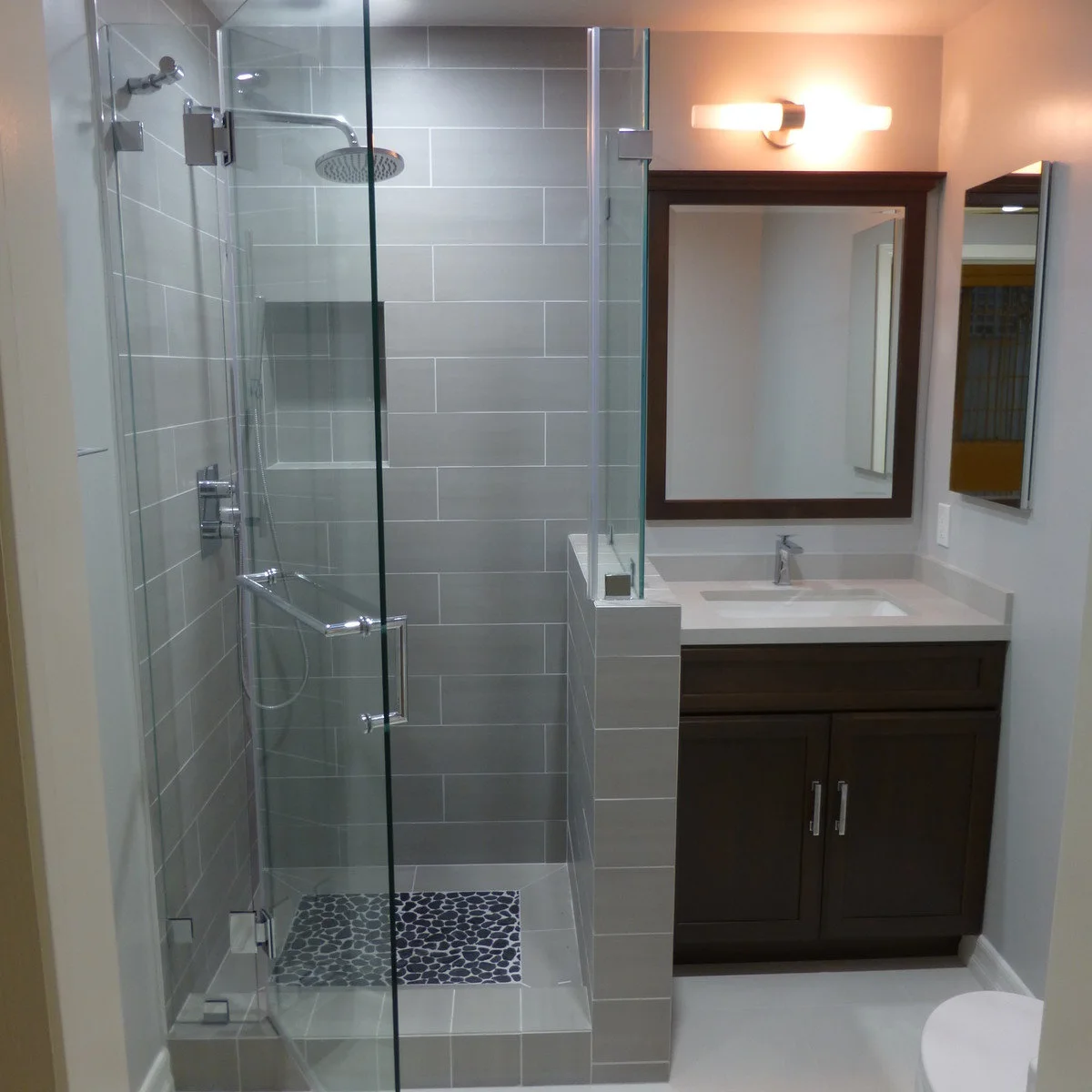 Compact bathroom with a short tiled partition between a glass shower and dark vanity