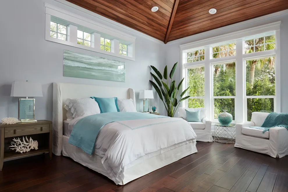A white bed with pale blue bedding stands on dark wood flooring beneath a timber ceiling